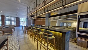 A modern bar area with a long counter and multiple stools, a kitchen with stainless steel appliances, and a seating area with sofas and a patterned rug. - Holiday Inn Mexicali Centro Civico by IHG (Mexicali)