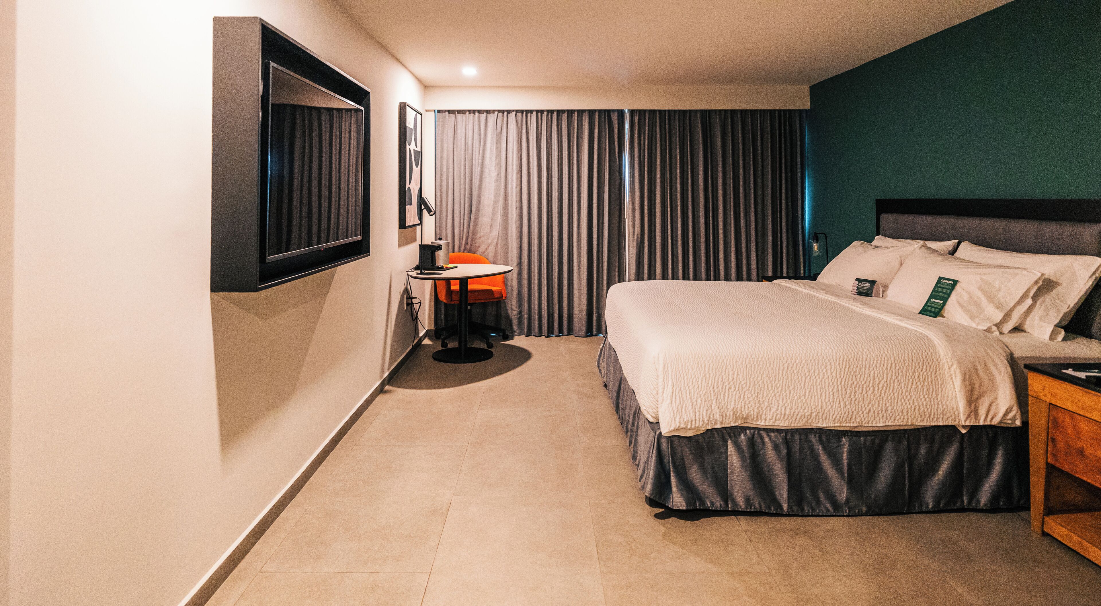A hotel room with a bed, a desk, a chair, a TV, and curtains.