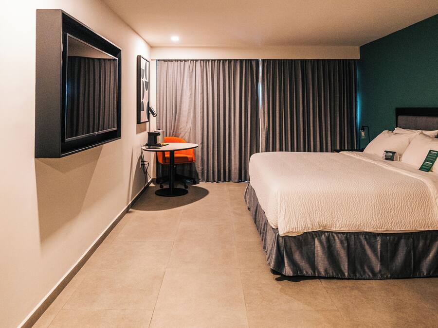A hotel room with a bed, a desk, a chair, a TV, and curtains.