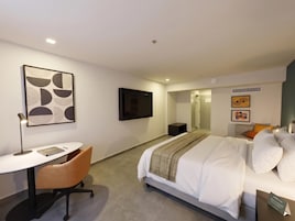 Habitación de hotel con cama, escritorio, silla, televisor y obras de arte en las paredes.