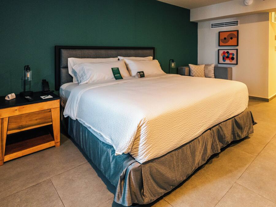 A hotel room with a bed, a nightstand, a lamp, and a wall with artwork.