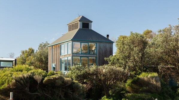 A modern house with a large glass window, surrounded by dense vegetation.