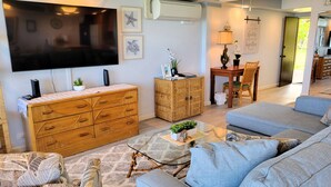 Een woonkamer met een televisie, een houten kast, een bank en een eethoek met een tafel en stoelen.