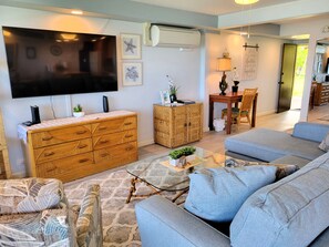 A living room with a television, a wooden cabinet, a sofa, and a dining area with a table and chairs. - Exquisite Direct Sunset & Oceanview 4 Miles! Pool (Lahaina)