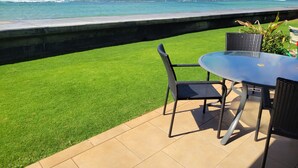 Een terras met tafel en stoelen, uitkijkend op een strand met golven.