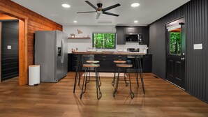 Una cocina moderna con una isla central, taburetes de bar, un refrigerador y un ventilador de techo.
