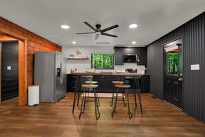 Eine moderne Küche mit einer zentralen Kochinsel, Barhocker, einem Kühlschrank und einem Deckenventilator.