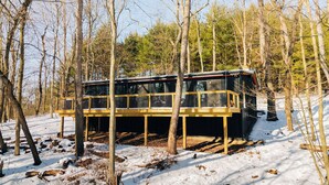 Una cabaña con terraza de madera, rodeada de árboles y nieve.