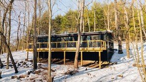 Eine Holzhütte mit einer Holzterrasse, umgeben von Bäumen und Schnee.