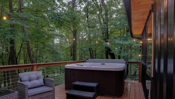Una terraza de madera con un jacuzzi, mobiliario de mimbre e iluminación con luces colgantes.