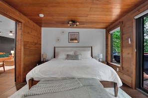 Quarto com teto de madeira, cama com roupa de cama branca, duas luminárias de cabeceira e um quadro na parede.