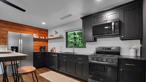 Una cocina moderna con armarios oscuros, electrodomésticos de acero inoxidable y una pared de acento de madera.