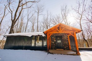 Eine Holzhütte mit Kamin aus Stein, einer überdachten Veranda und einem mit Schnee bedeckten Dach.