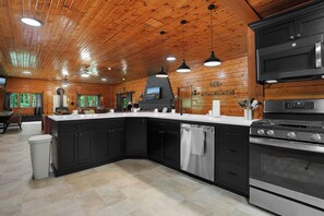 A modern kitchen with a large island, black cabinetry, stainless steel appliances, and a wooden ceiling. - The Lodge at Rivers Edge Retreat | Hot tub + Pickleball (Malvern)