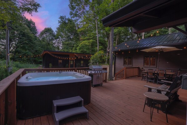 A wooden deck with a hot tub, outdoor furniture, and string lights. - The Lodge at Rivers Edge Retreat | Hot tub + Pickleball (Malvern)