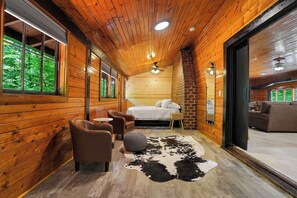 A log cabin interior with a bed, seating area, and a cowhide rug. - The Lodge at Rivers Edge Retreat | Hot tub + Pickleball (Malvern)