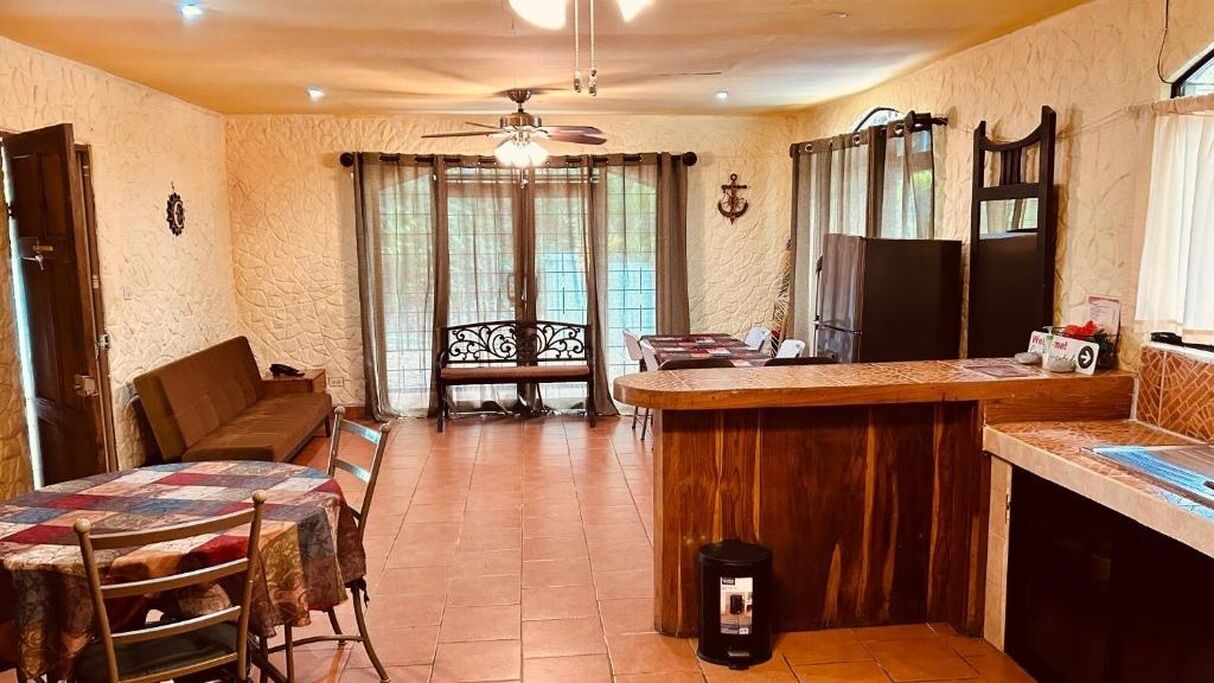 A cozy living room with a dining table, a sofa, and a kitchen area with a wooden counter and a refrigerator.