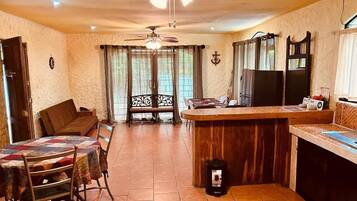 A cozy living room with a dining table, a sofa, and a kitchen area with a wooden counter and a refrigerator.