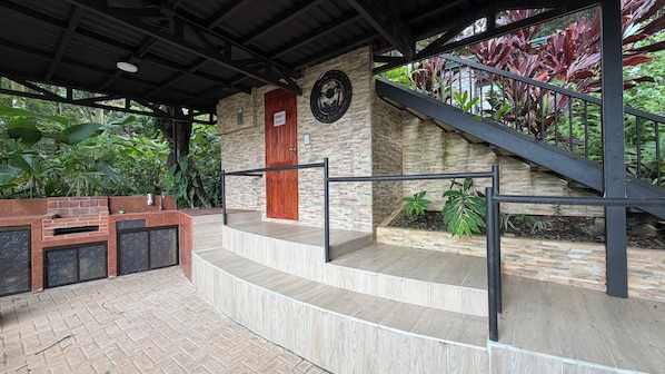 A covered outdoor area with a stone wall, a wooden door, and a metal staircase.