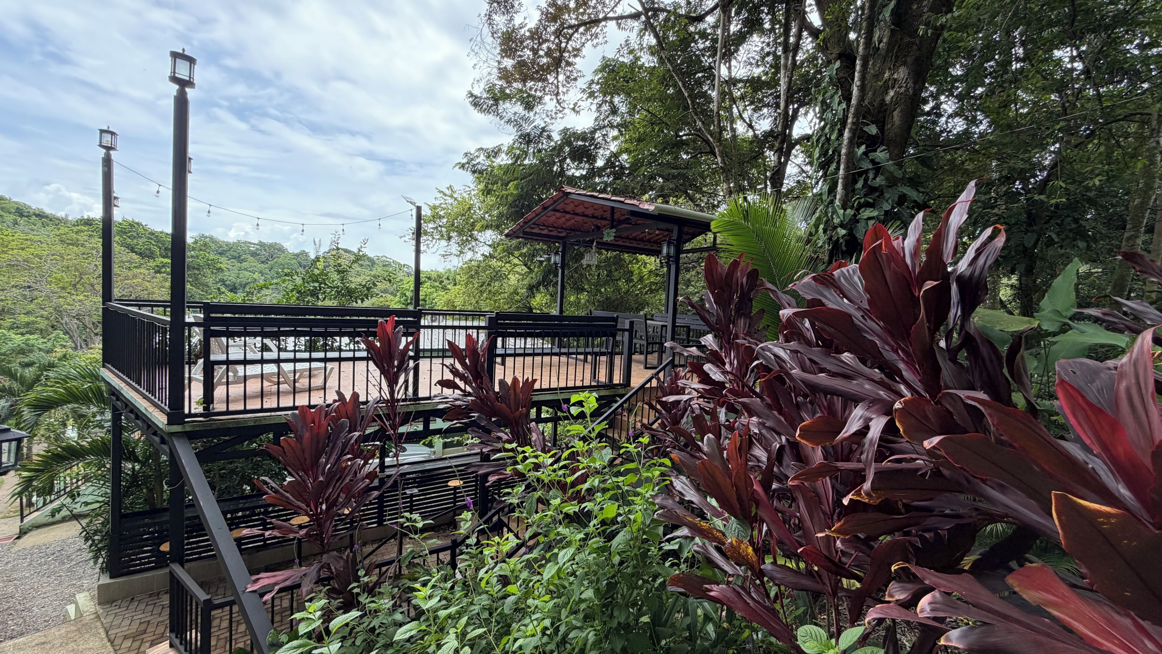 Un gazebo con tetto e panchina, immerso nel verde e con vista su una strada.