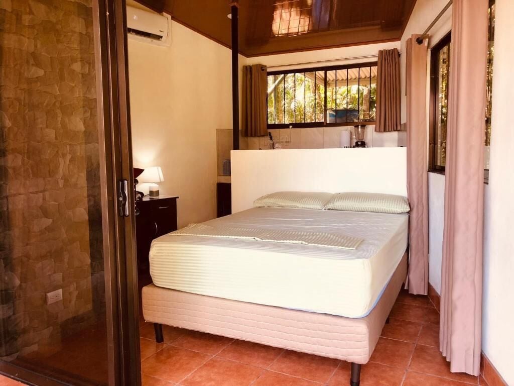 Een slaapkamer met een bed, nachtkastje, raam met gordijnen en een stenen muur.