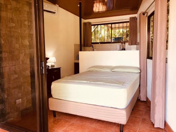 A bedroom with a bed, a nightstand, a window with curtains, and a stone wall.