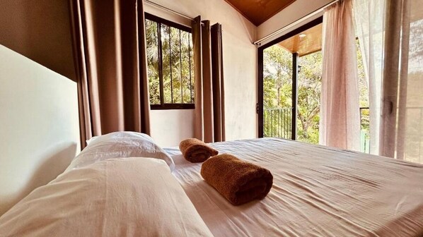 A hotel room with a bed, two rolled towels, and a view of greenery through the windows. - Casa Encantada (Quepos)