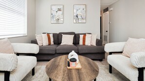 Ein Wohnzimmer mit grauem Sofa, weißen Sesseln, einem runden Couchtisch und zwei abstrakten Bildern an der Wand.