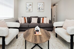 A living room with a grey sofa, white armchairs, a round coffee table, and two abstract paintings on the wall. - Stylish 2bed room Apt Near Hospitals Golf course and Beaches (St. Petersburg)