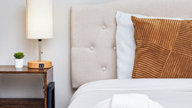 Ein Hotelzimmer mit Bett, Nachttisch mit Lampe, einer kleinen Pflanze und einem gefalteten Handtuch.