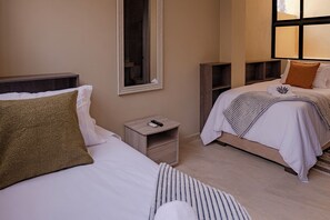 A hotel room with two beds, a nightstand with a remote control, a mirror, and a window with blinds. - Casa Maguey | Rooftop Jacuzzi, Bay Views & Culture (Cartagena de Indias)