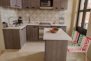 A kitchen with wooden cabinets, a tiled backsplash, a microwave, a sink, and a wooden bowl on the counter. - Casa Maguey | Rooftop Jacuzzi, Bay Views & Culture (Cartagena de Indias)