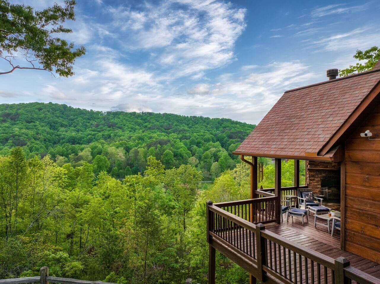 A wooden cabin with a deck and outdoor seating, surrounded by a forested landscape.