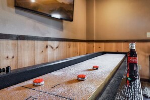 A shuffleboard table with three pucks, a bottle of Coca-Cola, and a television mounted on the wall. - Mountain Views • Hot Tub • Fire Pit • Games (Blue Ridge)