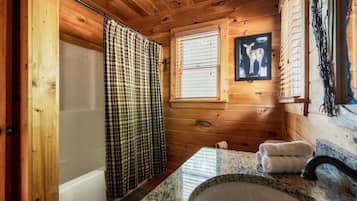 Ein Badezimmer einer Holzhütte mit Badewanne, Waschbecken und einem Fenster mit Jalousien.