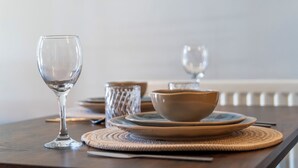 Uma mesa de jantar com um copo de vidro transparente, uma tigela, pratos e pauzinhos.