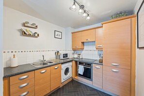 Una cocina moderna con armarios de madera, lavadora, horno, microondas y pileta.