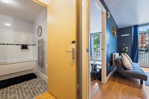 A hotel room with a bathtub, a wooden door, a grey sofa, and a view of the outside. - Central location| Private Patio|Free Parking|Wi-Fi (West Midlands)