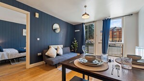 Uma sala de estar moderna com sofá, mesa de jantar e uma janela grande com vista para edifícios.