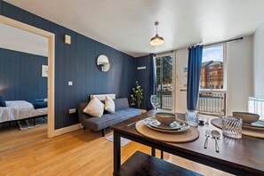 A modern living room with a sofa, dining table, and a large window with a view of buildings. - Central location| Private Patio|Free Parking|Wi-Fi (West Midlands)