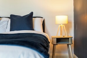 A bed with a dark headboard, white and dark pillows, and a bedside lamp on a small wooden nightstand. - Central location| Private Patio|Free Parking|Wi-Fi (West Midlands)