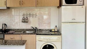 A compact kitchen with wooden cabinets, a microwave, a dishwasher, and a washing machine. - Recharge in this peaceful and stylish place. (Funchal)