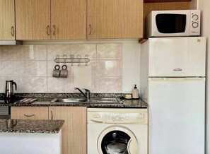 A compact kitchen with wooden cabinets, a microwave, a dishwasher, and a washing machine. - Recharge in this peaceful and stylish place. (Funchal)