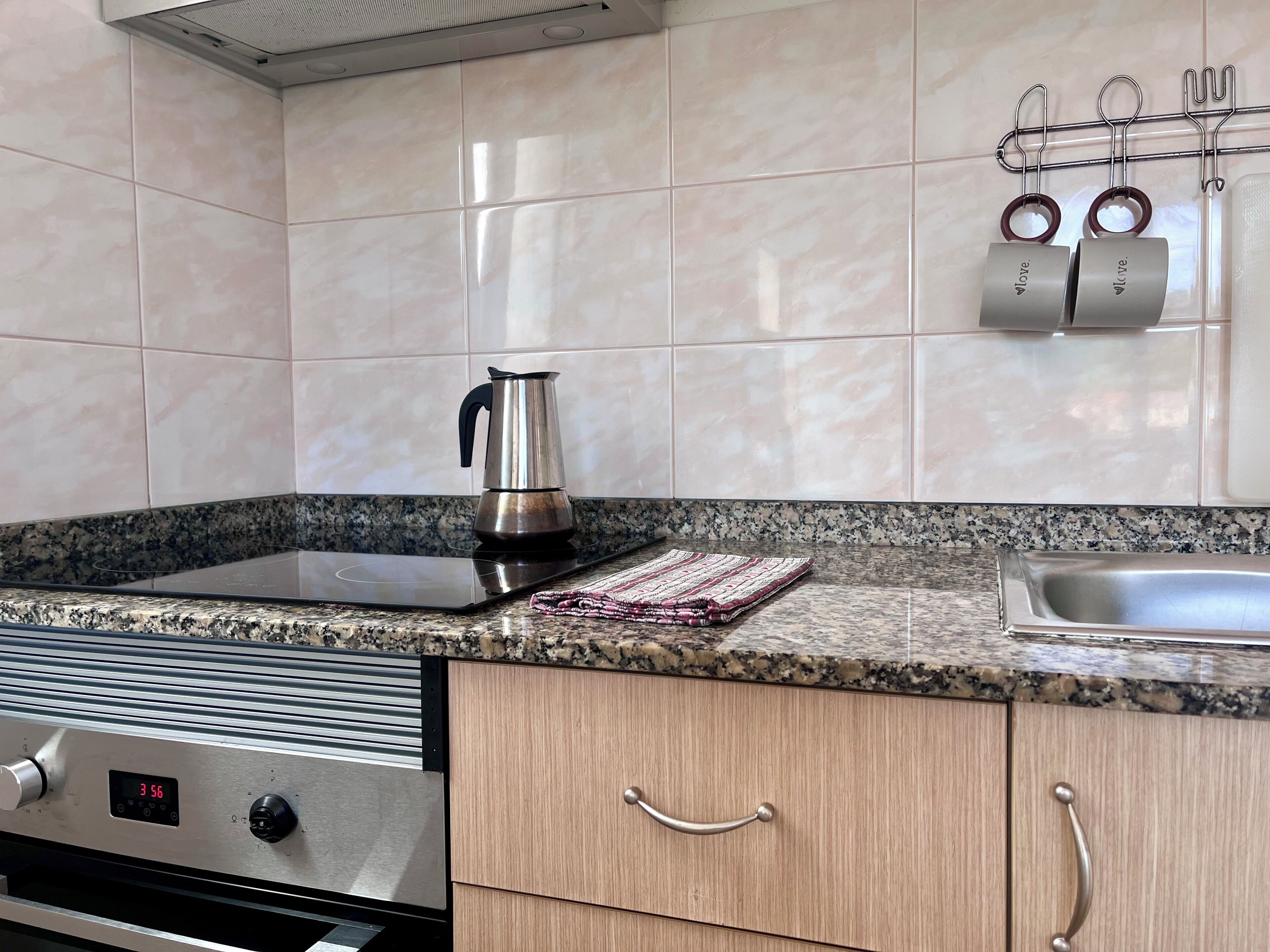A kitchen with a stainless steel kettle, a granite countertop, a built-in oven, and a wall-mounted spice rack.