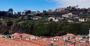 A hillside residential area with terraced houses, some with red-tiled roofs, and a mix of modern and traditional architecture. - Recharge in this peaceful and stylish place. (Funchal)