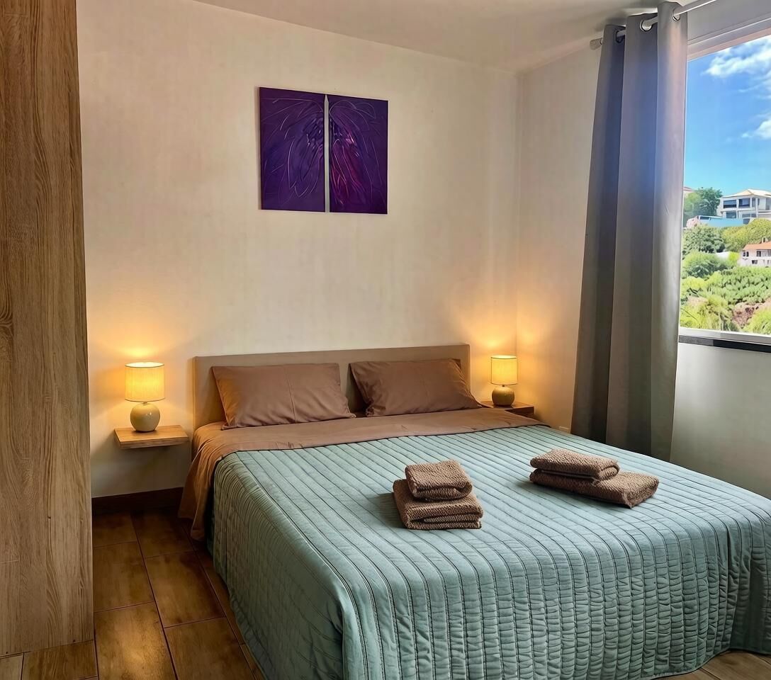 Ein Hotelzimmer mit einem Bett, zwei Nachttischlampen, einem Fenster mit Vorhängen und einem Bild an der Wand.