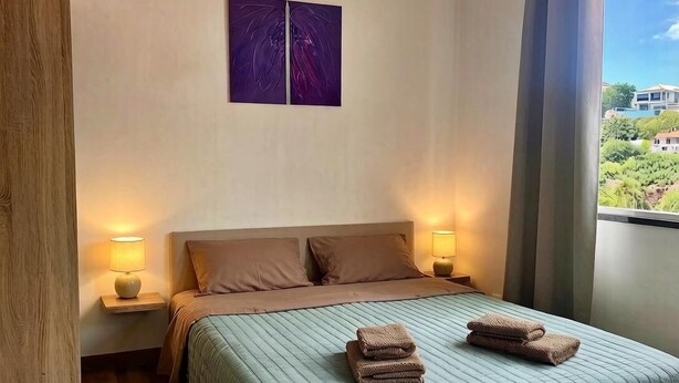 A hotel room with a bed, two bedside lamps, a window with curtains, and a painting on the wall. - Recharge in this peaceful and stylish place. (Funchal)