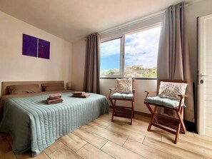 A bedroom with a bed, two chairs, a window with curtains, and a view of the outside. - Recharge in this peaceful and stylish place. (Funchal)