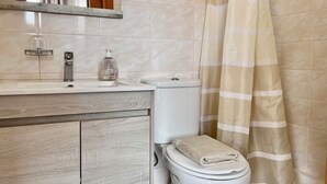 A bathroom with a toilet, sink, mirror, and shower curtain. - Recharge in this peaceful and stylish place. (Funchal)