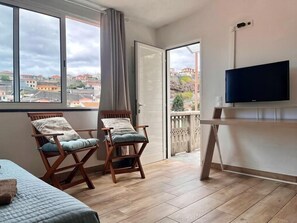 A room with a bed, two chairs, a television, and a balcony with a view of buildings. - Recharge in this peaceful and stylish place. (Funchal)